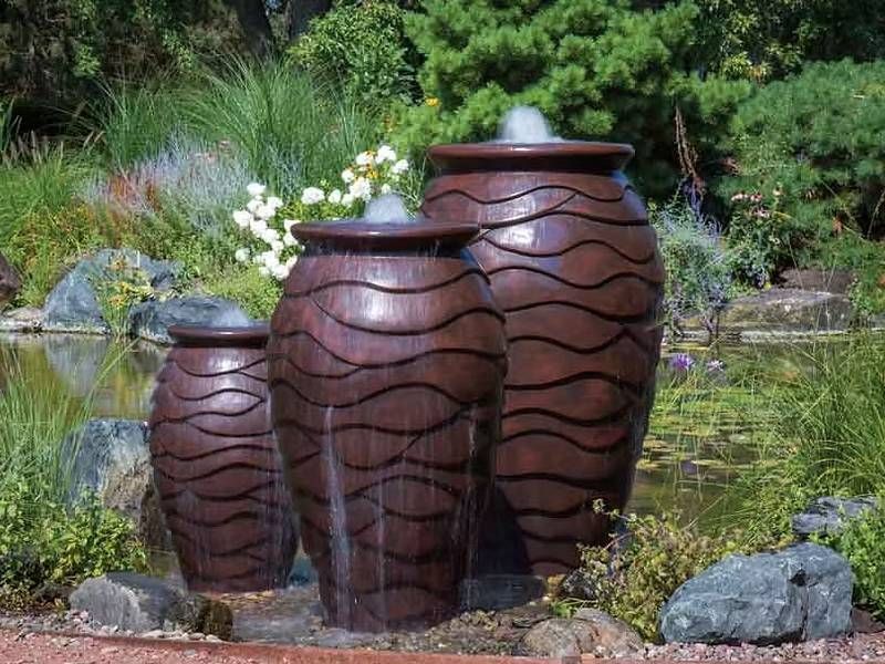 Three tall ribbed urn fountains beside a planted pond