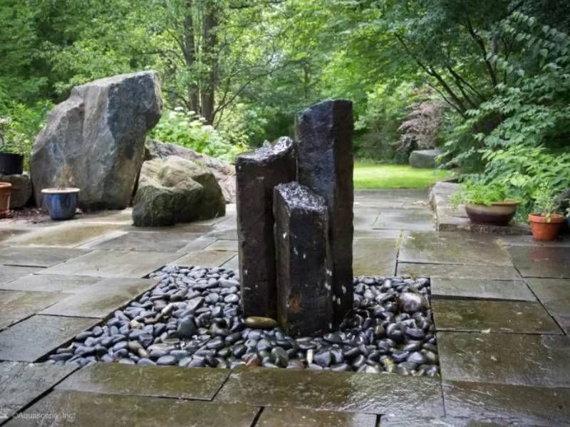 Basalt column fountain in a pebble bed on a stone patio