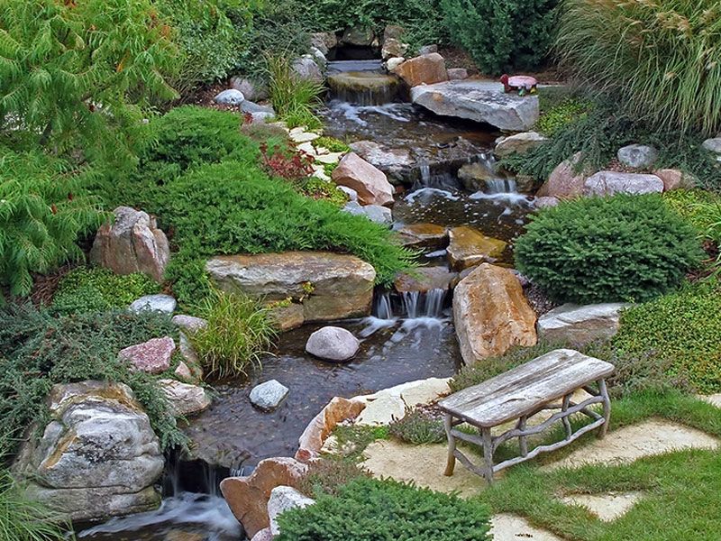 Stream and waterfall with a wooden bench among shrubs