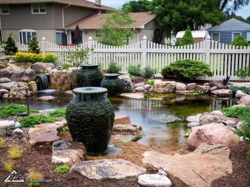 Pond with a slate urn fountain beside a white picket fence
